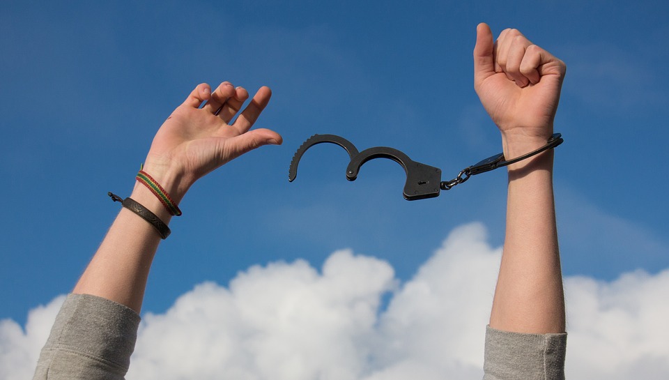 freedom from addiction. man breaking free of handcuffs with clouds in the backdrop