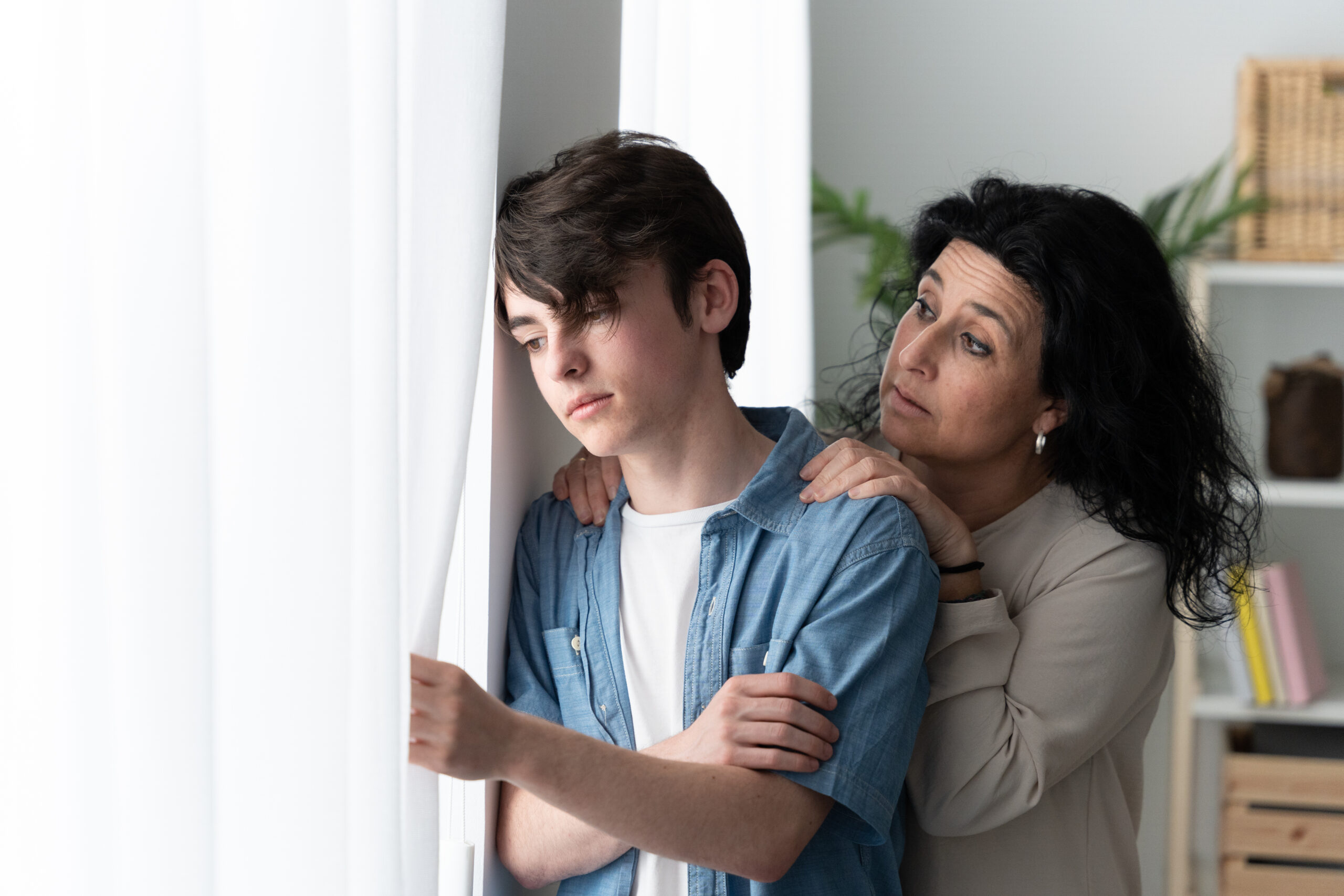 mother showing concern for son who is looking out the window. Signs of drug use in children, concept image.